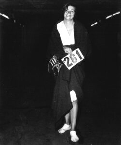 Kathrine Switzer stands with bloody feet but smiling, holding her '261' race number after completing Boston 67. 