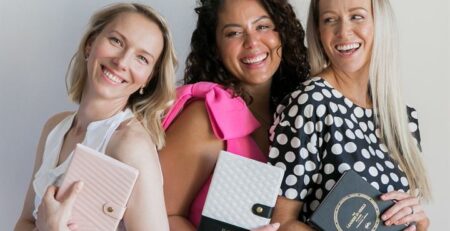 A support network of women stand together smiling, holding LH Agenda journals.