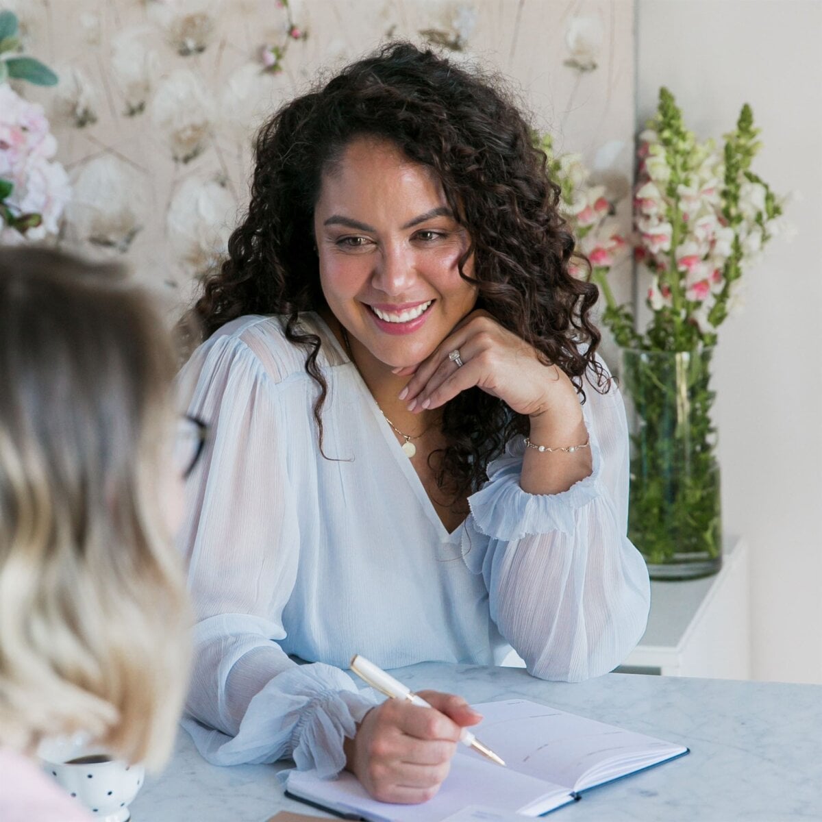 Woman sits with her boss negotiating a pay rise, her notebook and pen in hand.